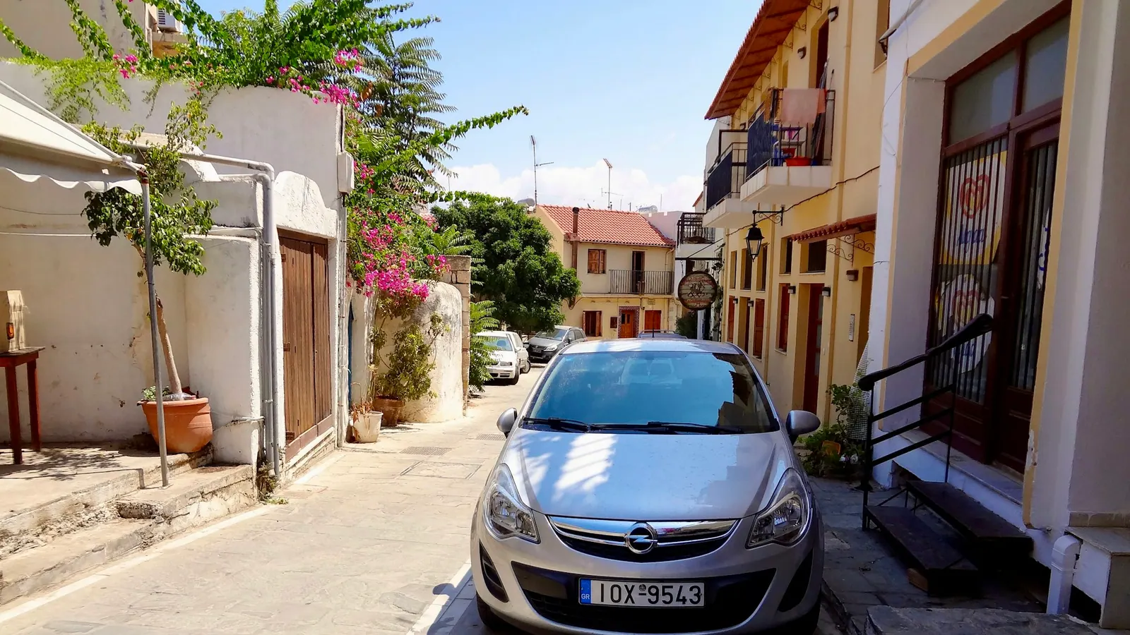 Ασημί αυτοκίνητο με ελληνικές πινακίδες, παρκαρισμένο σε στενό ελληνικού χωριού.
