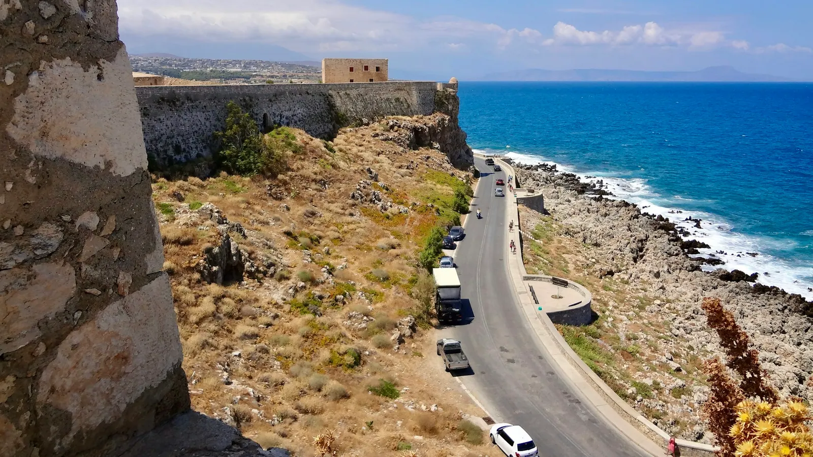 Παραλιακός δρόμος με αυτοκίνητα, κάτω από βενετσιάνικο κάστρο.