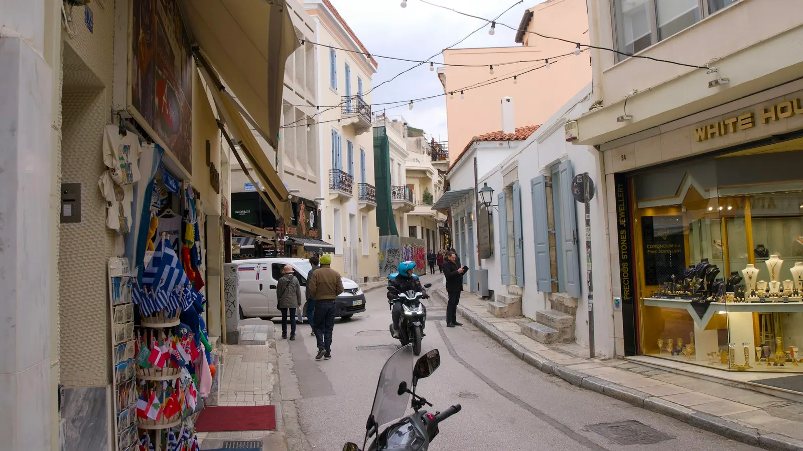 Σκούτερ σε εμπορικό δρόμο ελληνικής πόλης, ανάμεσα σε μαγαζιά.