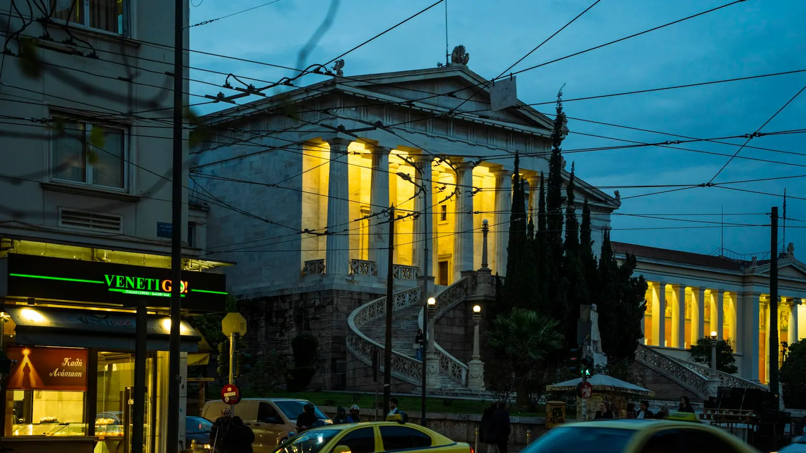 Κίτρινα ταξί μπροστά από νεοκλασικό κτίριο της Αθήνας, το σούρουπο.